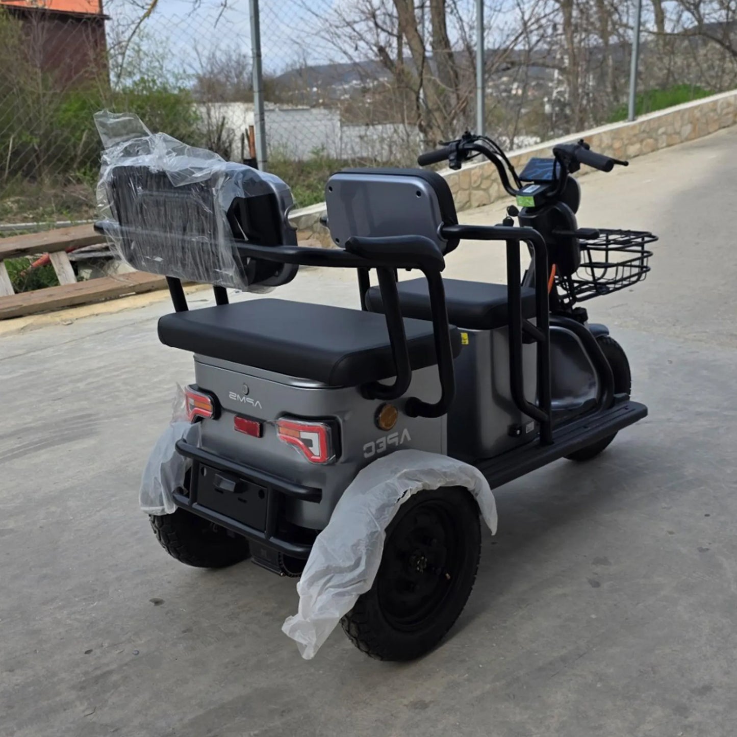 Vedere din spate în exterior a tricicletei electrice Grande gri, pregătită de drum.